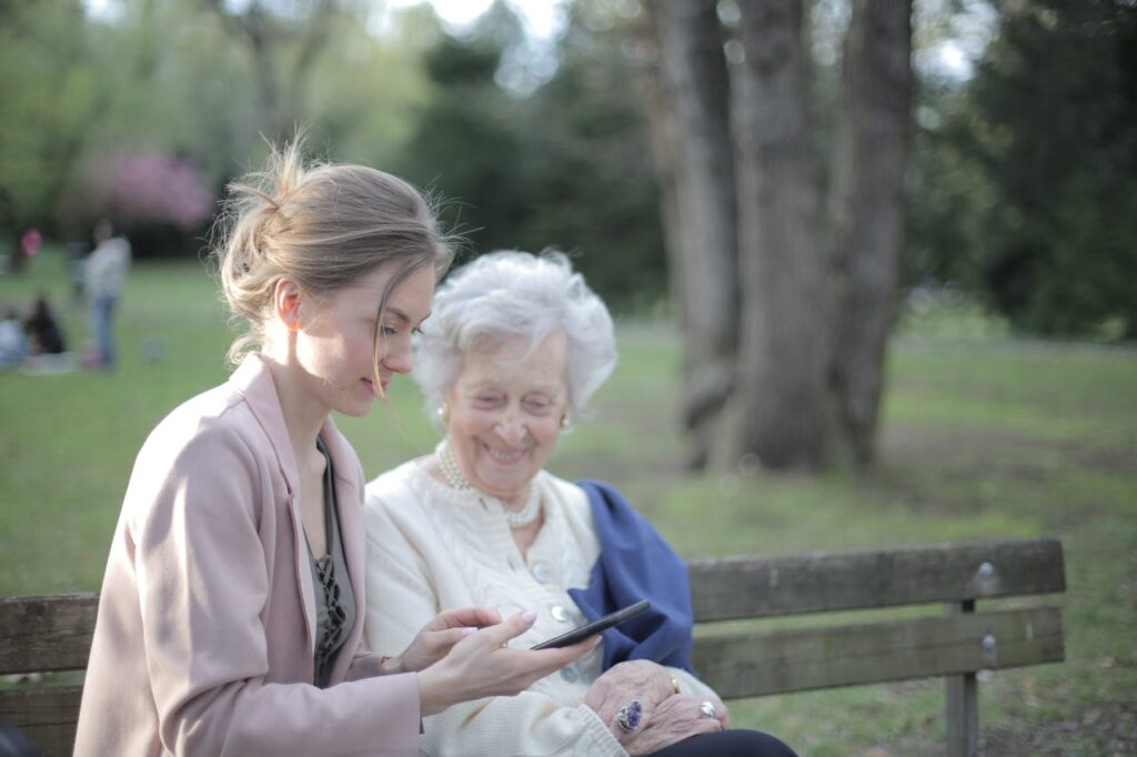 pexels-photo-3791666 Side view of smiling adult female helping aged mom in using of mobile phone while sitting together in park